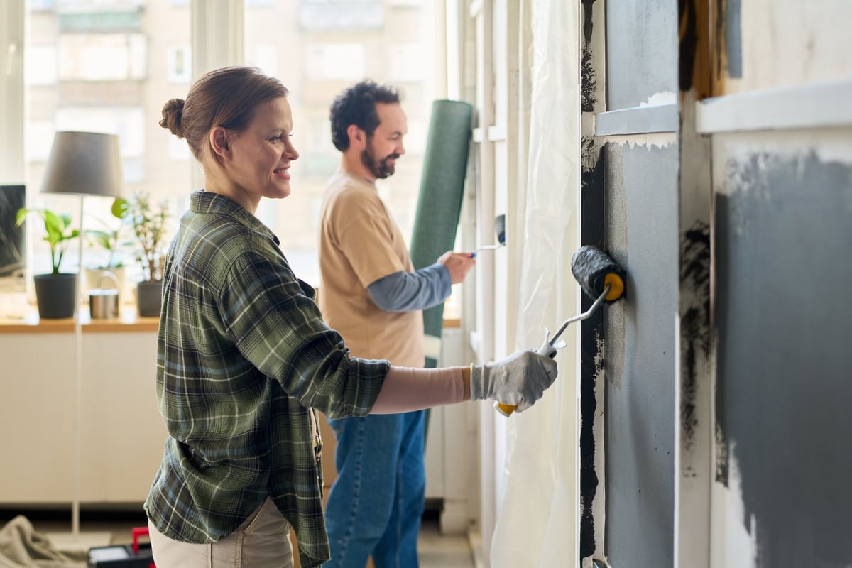 Mujer aplicando pintura gris con rodillo en el salón de su vivienda