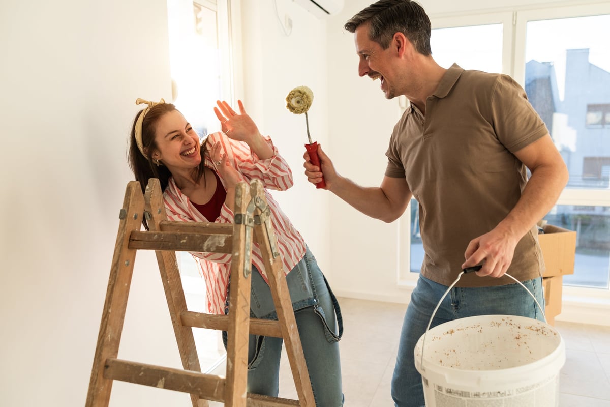 Pareja pintando juntos las paredes de una habitación con rodillo
